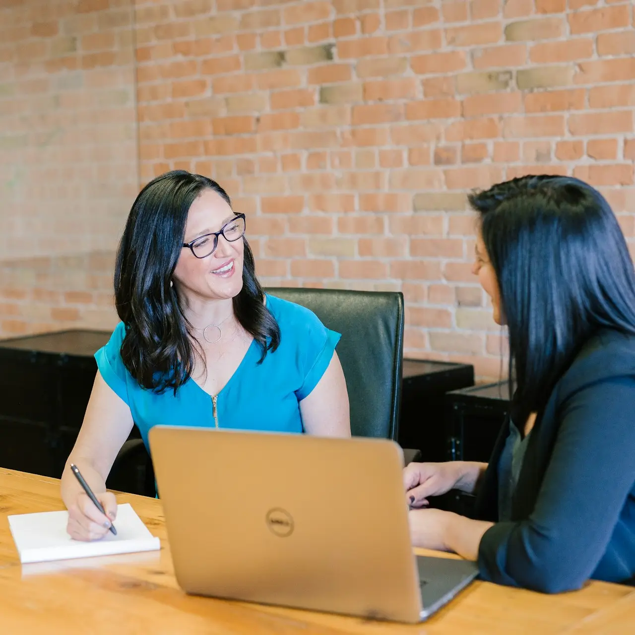 woman in teal t-shirt sitting beside woman in suit jacket